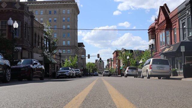 Long angle hand held shaky video of two yellow lanes going down the middle of the street on a sunny day with white clouds in the sky in a midwestern city in urban downtown setting.