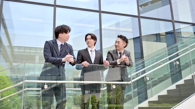 屋外のビル背景で未来を見据え笑顔で語る会社のビジネスマンチームの成長と挑戦　プロジェクトの成功などのポジティブ前向き上司、部下など3人チームのイメージの動画