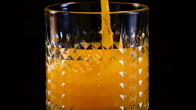 Orange Juice Pouring into a Textured Crystal Glass on Black Background