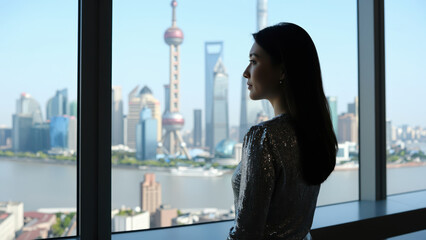 Fototapeta premium Cityscape contemplation: A graceful silhouette gazes out from a modern window at a cityscape of skyscrapers and iconic towers, invoking a sense of aspiration and introspection.