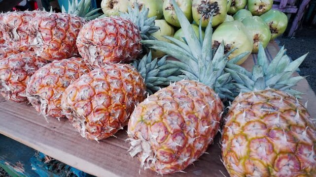 Row of fresh pineapples and pile of green coconuts on display at local fruit market