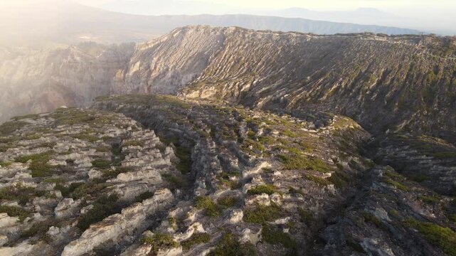 Cinematic drone half orbit along the edge of Kawah Ijen volcanic crater at golden hour East Java Indonesia revealing dramatic sulphur lake and crater rim