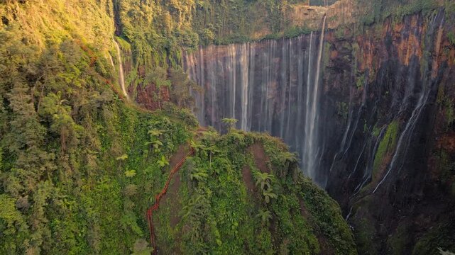 Cinematic drone flyover small hill dramatically revealing the stunning Tumpak Sewu waterfall canyon in East Java Indonesia lush tropical jungle landscape