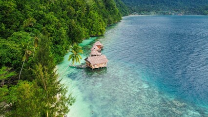 Serene Overwater Bungalows Surrounded by Tropical Rainforest and Crystal Clear Sea in Maluku. © ferdi