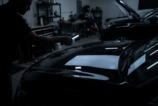Spray of water and droplets cascading off dark car body during professional detailing wash drying with water sheeting