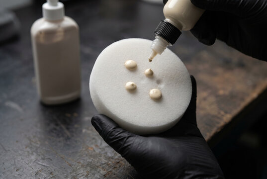Detailer hand priming white foam polishing pad with cream compound drops paint correction preparation close up macro