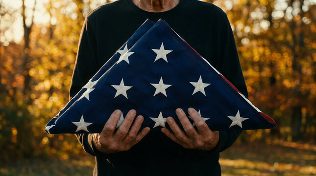 Veteran holding a folded American flag during an autumn memorial ceremony to honor the sacrifice and service of military personnel.