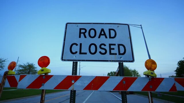 Blocked road with barricades and warning sign Road CLOSED with blinking lights at dusk showing restricted access and construction area. Wide view Close up