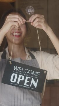Vertical Screen : Young Asia manager girl changing a sign from closed to open sign on door cafe looking waiting for clients after lockdown. Owner small business, food and drink, business reopen again.