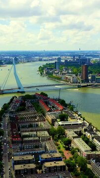 Vertical video. Rotterdam, Netherlands. Erasmus Bridge with its 139-meter asymmetrical white pylon spanning the Nieuwe Maas River, Drone footage over Noordereiland and the modern skyline under a part