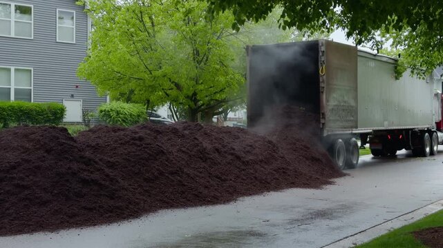 Truck unloading large pile of fresh mulch in residential neighborhood for landscaping project. Lawn care and garden maintenance service concept.
