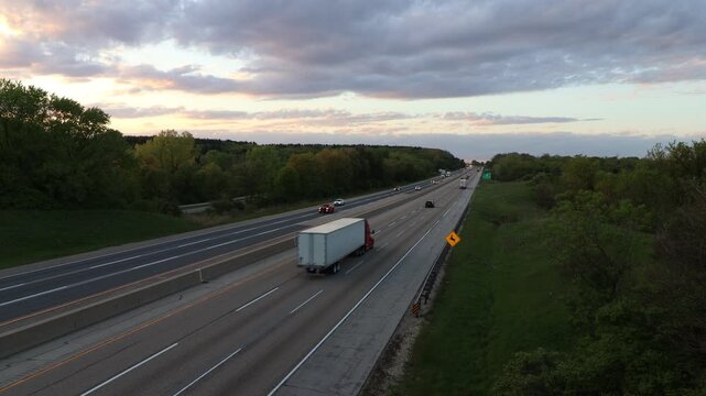 Cars and semi trucks drive down a long interstate highway road into the horizon in the top right third of the screen.