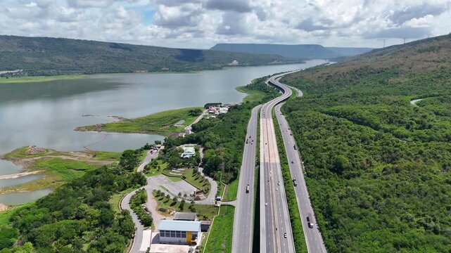 Aerial view of highway running along river and green hills. Transportation, infrastructure, travel and logistics concept