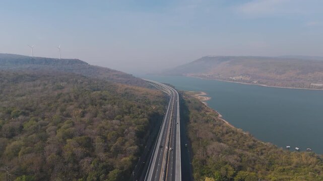 Aerial view of highway running along river and green hills. Transportation, infrastructure, travel and logistics concept