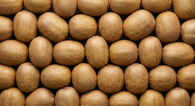 A dense arrangement of ripe brown kiwifruits with fuzzy skin, showcasing their oval shapes and natural texture in a repeating pattern for a food background