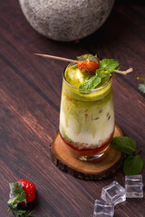a glass of strawberry matcha drink containing strawberry jam, full cream milk, matcha and strawberries with strawberry and mint leaf decoration on a wooden coaster © kitapoto
