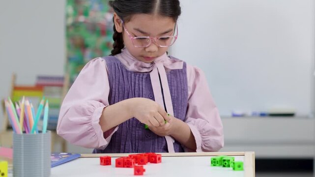 Young Asian Girl Counting and Connecting Colorful Math Blocks in Classroom