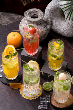 A glass of lemon mojito, mango mojito, and strawberry mojito with a composition of lemon syrup, soda, and ice cubes, plus toppings of lemon slices, mint leaves, and basil seeds, in a glass with a roun