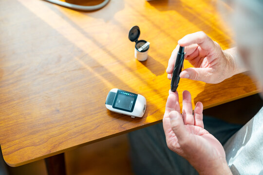 Senior man checking blood sugar level with glucose meter at home, elderly person using lancet device for diabetes monitoring and daily healthcare management during wellness routine