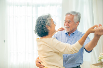 Obraz premium Happy Asian senior couple dancing together at home, elderly husband and wife enjoy active retirement lifestyle indoors, loving older people spending time together, healthy aging joyful relationship.