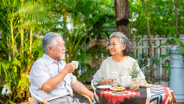 Happy Asian family senior couple enjoy afternoon tea together in the garden, elderly husband and wife relaxing outdoors during retirement lifestyle, healthy aging older spending quality time at home