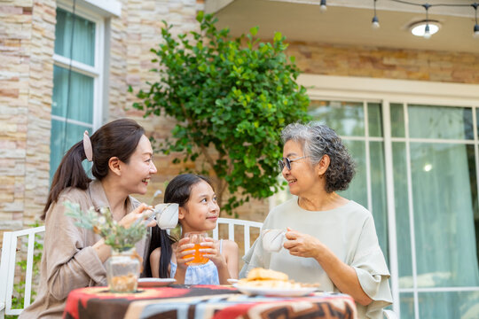 Happy Asian grandmother, mother and young girl having afternoon tea party spending time together at home. Multi-generation women family enjoy weekend activities outdoor lifestyle in the garden