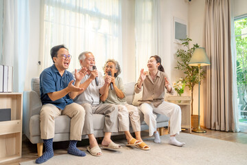 Obraz premium Happy multi-generation Asian family singing karaoke together at home, senior parent and adult child enjoy and fun leisure activity in living room, family bonding, happiness joyful retirement lifestyle