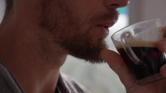 A mature man with a goatee drinking coffee from a transparent teacup, stationary