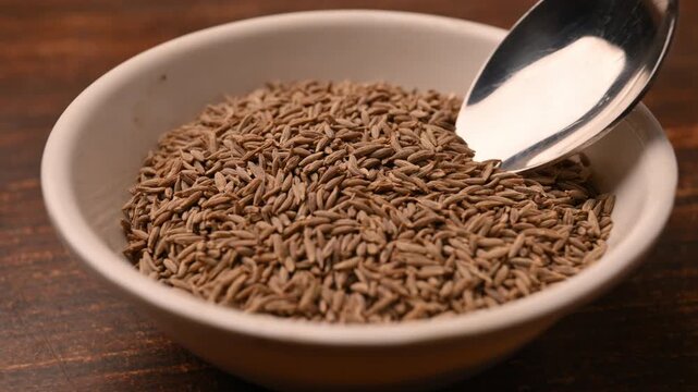 Cinematic 4K Macro Shot of Cumin Seeds Being Scooped with Spoon from Bowl on Table in Angled Top View with Soft Blur Background
