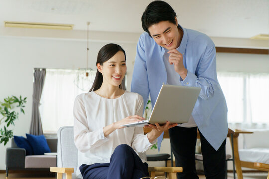 リビングでノートパソコンを持って会話する若い日本人セレブカップル