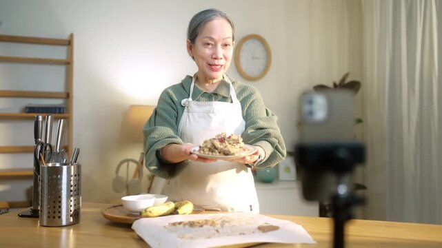 Senior woman livestreams cooking from home on smartphone, highlighting active aging and digital lifestyle. Reflects social media, content creation, creativity, and senior lifestyle.