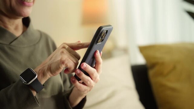 Senior woman controlling smart home lighting with smartphone, turning on lamp via mobile app, home automation, digital lifestyle, connected living, independent living, active aging and technology.