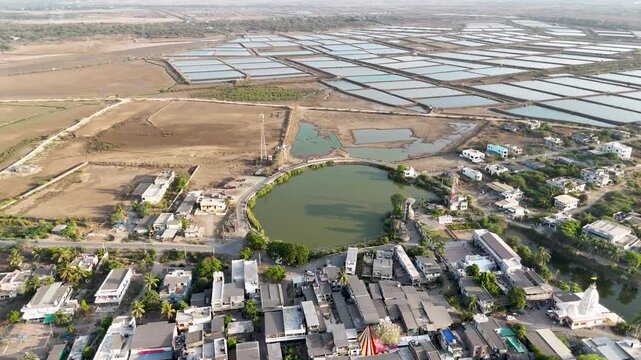 A breathtaking aerial view of expansive salt evaporation ponds spread across a dry coastal landscape near a rural village.