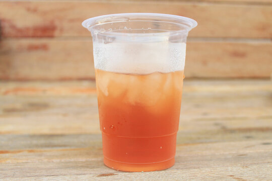 Cold iced tea in a plastic cup with condensation on wooden background, refreshing summer beverage concept