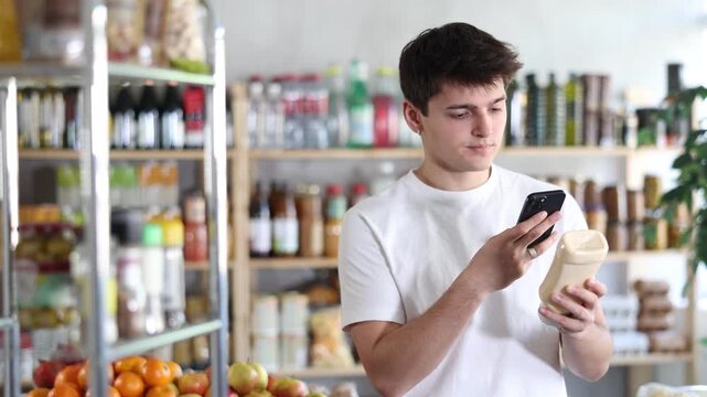 Male buyer checks suitability - scans QR code on jar of mayonnaise label in a grocery store. High quality 4k footage
