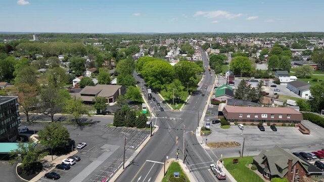 High angle drone footage capturing a complex five way road intersection with traffic flow and surrounding commercial retail buildings on a sunny day.