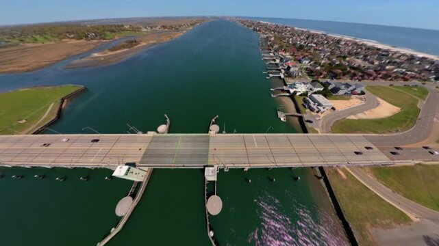 An FPV drone point of view over the Atlantic Beach Bridge on a sunny day. The camera dolly out and tilt down over the bridge. Vehicles and the blue sky is visible,.