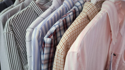 Selection of various mens button down shirts with patterns and stripes hanging on a clothing rack in a retail store for professional business casual fashion style © Rungphailin