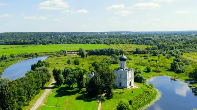 Russia, Bogolyubovo. Church of the Intercession on the Nerl, a white-stone Orthodox church with a single dark dome, Drone footage over the Nerl River floodplain in summer. Drone footage, Point of int