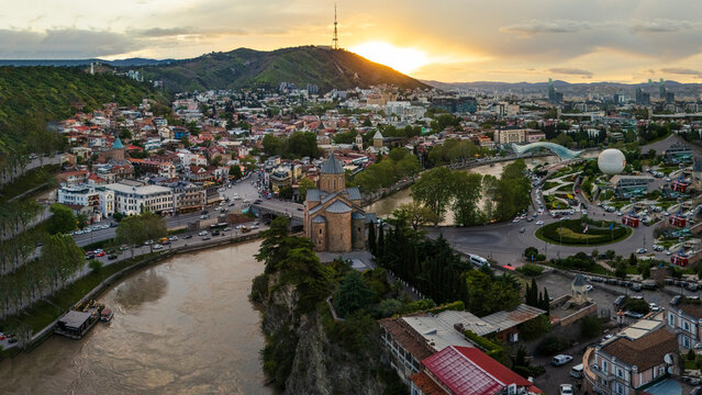 Aerial view of Tbilisi at sunset with Metekhi Church, Bridge of Peace and Rike Park. Golden hour over the Georgian capital showing Mtkvari River and the skyline of the historic city center