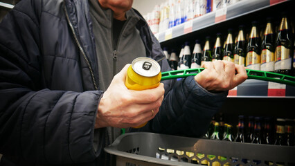 Close-up of a customer's hand putting a can of beer into a shopping cart © Stockah