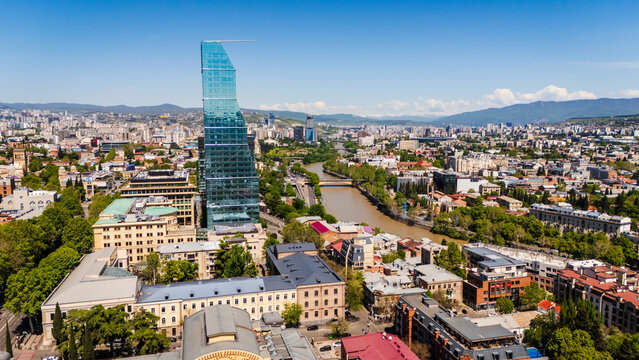 Aerial view of the modern Biltmore Hotel skyscraper and the Mtkvari River in Tbilisi, Georgia. Cityscape panorama featuring contemporary glass architecture and the urban skyline at daytime