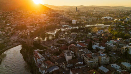 Aerial sunset view of Metekhi district in Tbilisi, Georgia, featuring historic houses on the Kura River cliffs with warm golden hour light over the city © Michele
