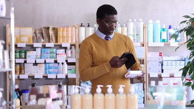 African man in pharmacy scans QR code on pills, studies item in detail, collects information online, uses quick link to access drugs instructions. 