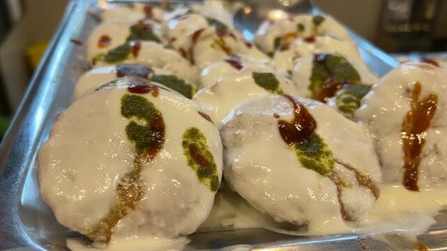 A delicious, close-up shot of a loaded plate of Dahi Bhalla, overflowing with chilled thick yogurt, sweet tamarind sauce, and fresh coriander leaves