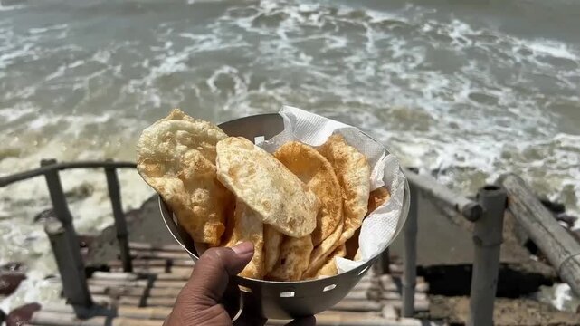 A man holding fresh dal puri in front of waves in sea beach