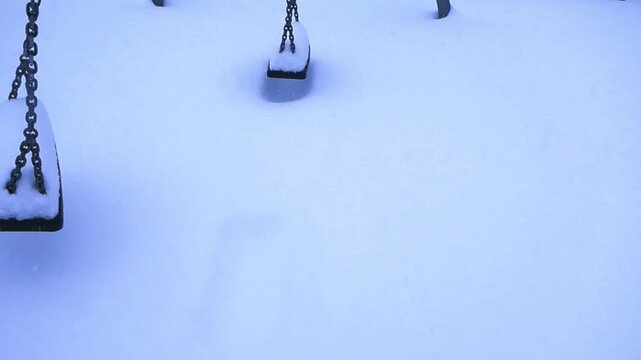 Empty Playground Swings Moving in the Winter Snow