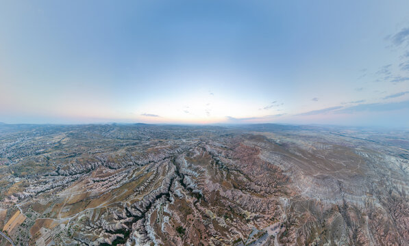 Goreme, Nevsehir, Turkey. Wide panoramic aerial view of Cappadocia plateau after sunset, with soft pink and orange afterglow over eroded valleys and distant ridges. Aerial view.