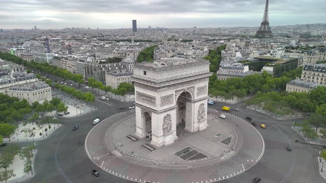 Aerial view of the famous landmark Triumphal Arch or Arc de Triomphe and Eiffel Tower surrounded by busy streets and lush greenery in the heart of the city Paris, France. Aerial drone orbiting flight