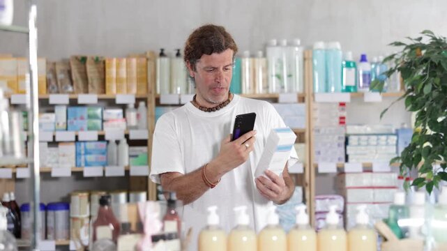 Adult man holds a mobile and scans the barcode of a cream in a European pharmacy. Purchase and payment for cosmetic products using a qr code. High quality 4k footage
